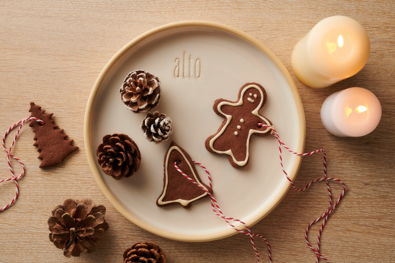 Teller mit Lebkuchen, Tannenzapfen und brennenden Kerzen auf Holztisch.